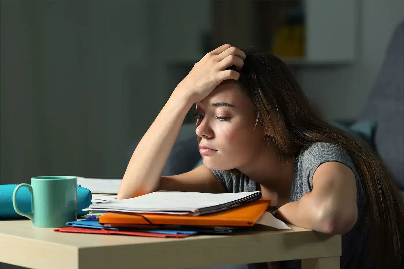 Eine Schülerin sitzt mit traurigem und erschöpftem Blick an ihrem Schreibtisch vor Schulbüchern.