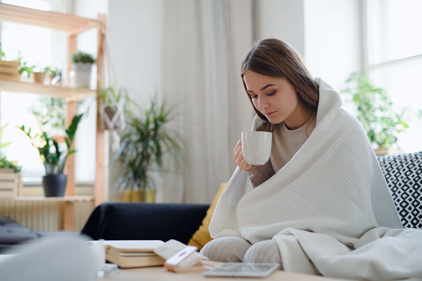 Eine junge Frau genießt in eine warme Decke eingekuschelt ein Heißgetränk.
