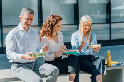 Drei Kollegen sitzen in ihrer Mittagspause zusammen draußen und essen ihr mitgebrachtes Mittagessen.