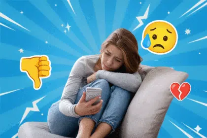 Eine junge Frau sitzt auf einem Sofa und schaut traurig auf ihr Handy.