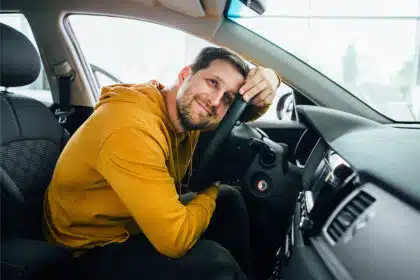 Ein Mann sitzt im Auto und umarmt verliebt sein Lenkrad.