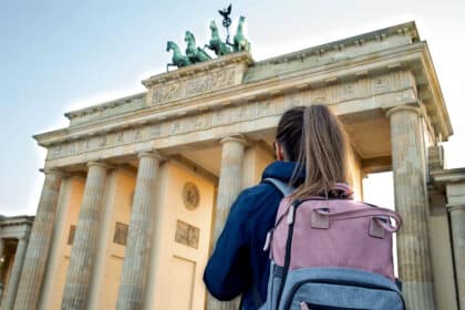 Eine Person mit Rucksack steht vor dem Brandenburger Tor in Berlin und blickt nach oben auf das historische Bauwerk.