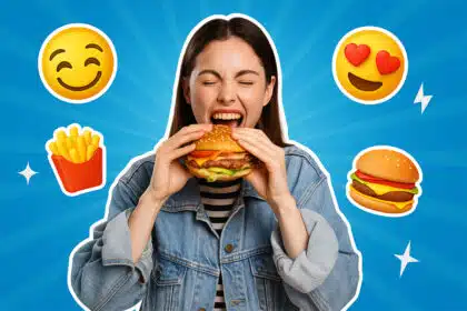 Junge Frau beißt lachend in einen Burger, umgeben von blauen Hintergrund und 3D-Emojis.
