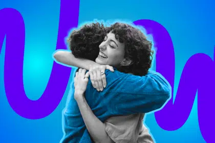 Zwei Personen umarmen sich herzlich und lächeln, vor einem leuchtend blau-lila Hintergrund.