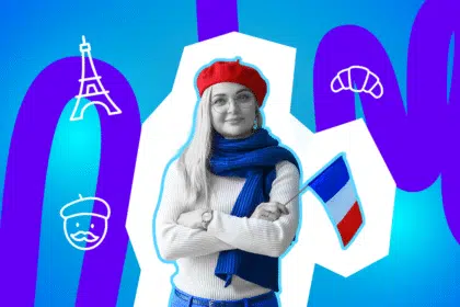 Frau mit rotem Barett und blauem Schal hält eine kleine französische Flagge und steht mit verschränkten Armen vor buntem Hintergrund.