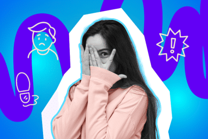 Frau in rosa Pullover verdeckt verlegen ihr Gesicht mit den Händen und blickt durch die Finger hindurch.