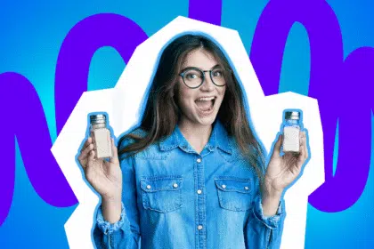 Junge Frau mit Brille hält lachend zwei Salzstreuer in den Händen vor bunt-blauem Hintergrund.