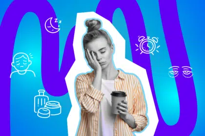 Eine müde junge Frau hält einen Kaffeebecher in der Hand und stützt erschöpft ihr Gesicht ab.