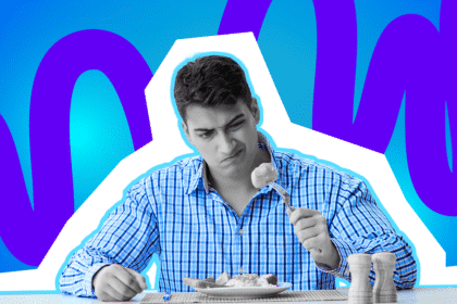 Mann sitzt am Tisch und blickt skeptisch auf ein Stück Essen auf seiner Gabel, das über seinem Teller gehalten wird.