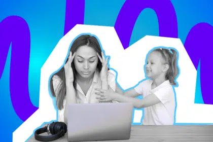 Gestresste Frau sitzt vor einem Laptop, während ein fröhliches Kind sie antippend Aufmerksamkeit sucht.