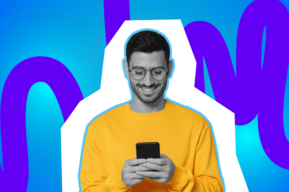 Lächelnder Mann im gelben Pullover schaut auf sein Smartphone und tippt, vor farbigem blau-violettem Hintergrund.