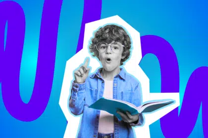 Kleiner Junge mit Brille hat ein Buch in der Hand und hält einen Zeigefinger in die Luft.