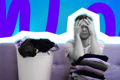 Gestresster Mann sitzt mit Wäschebergen auf dem Sofa und hält verzweifelt den Kopf in den Händen vor einem bunten, grafischen Hintergrund.
