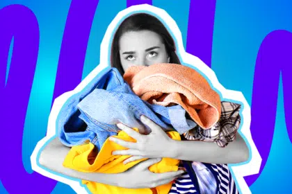 Humorvolle Collage zum Thema Haushalts-Frust und Wäsche waschen: Eine völlig überfordert und genervt dreinblickende Frau in Schwarz-Weiß verdreht resigniert die Augen nach oben. Sie trägt einen riesigen, chaotischen Berg aus knallbunter Kleidung (darunter eine blaue Jeans, ein orangefarbenes Handtuch und ein leuchtend gelber Pullover) in den Armen, hinter dem sie sich fast verstecken muss. Das Pop-Art-Motiv vor einem markanten blau-violetten Wellen-Hintergrund visualisiert pointiert den endlosen, ermüdenden Kreislauf der nervigsten aller Haushaltsaufgaben.