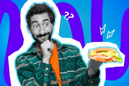 Ausdrucksstarke Collage zum Thema toxische Online-Diskussionen: Ein nachdenklich und skeptisch blickender Mann in Schwarz-Weiß fasst sich ans Kinn und betrachtet verwundert ein buntes, belegtes Sandwich in seiner ausgestreckten Hand. Er trägt ein leuchtend orangefarbenes T-Shirt unter einem grün gemusterten Hemd. Weiße Fragezeichen, Blitz-Icons und das Pop-Art-Motiv vor einem blau-violetten Wellen-Hintergrund visualisieren pointiert die völlige Verwirrung über eskalierende Social-Media-Kommentare und absurde Hassrede bei alltäglichen Themen.