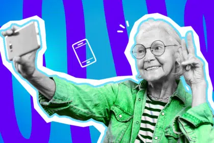Humorvolle Collage zum Thema Senioren und Digitalisierung: Eine fröhlich lächelnde, ältere Dame in Schwarz-Weiß mit runder Brille macht ein Selfie mit ihrem Smartphone und zeigt dabei entspannt das Peace-Zeichen. Sie trägt eine leuchtend grüne Jacke über einem gestreiften Shirt, was einen starken farblichen Kontrast erzeugt. Ein weißes Smartphone-Icon und das Pop-Art-Motiv vor einem markanten blau-violetten Wellen-Hintergrund visualisieren pointiert die moderne, technikaffine Großmutter-Generation, die beim Thema Apps und kontaktloses Bezahlen so manchen Jüngeren völlig lässig in den Schatten stellt.