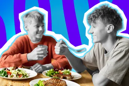 Emotionale Collage zum Thema Gastfreundschaft, gemeinsames Essen und Nächstenliebe: Auf der linken Seite sitzt eine lächelnde Person in Schwarz-Weiß, die ein Glas hält und einen leuchtend orangefarbenen Pullover trägt, der farblich stark hervortritt. Ihr gegenüber auf der rechten Seite sitzt eine weitere fröhliche Person im Profil in Schwarz-Weiß. Sie trägt ein beigefarbenes T-Shirt und hält eine Gabel in der Hand. Vor ihnen auf dem Holztisch stehen üppig gefüllte, bunte Teller mit frischem Salat und gebratenem Fleisch. Das Pop-Art-Motiv vor einem markanten blau-violetten Wellen-Hintergrund visualisiert pointiert das wärmende Gefühl von Zusammenhalt, das unkomplizierte Teilen einer Mahlzeit und den Moment, in dem ein Platz am Esstisch für jemanden freigemacht wird.